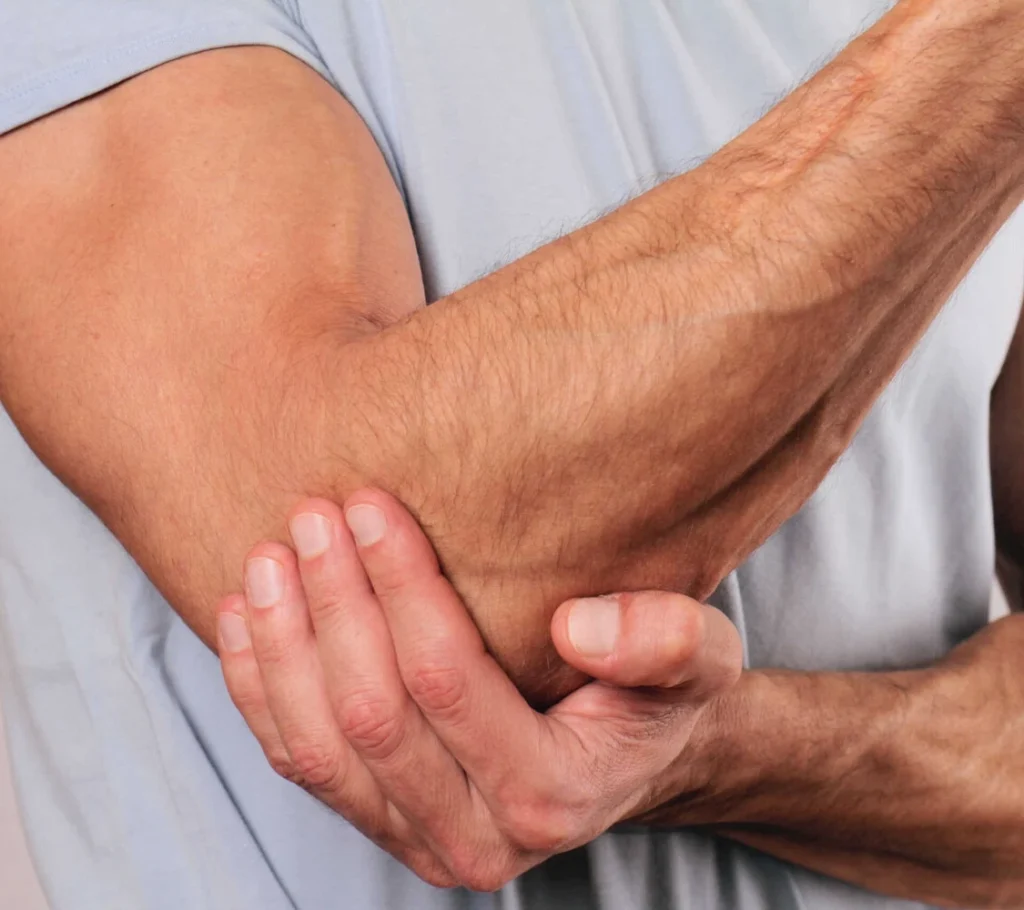 Man holding his injured elbow joint due to elbow pain - Greenlight Chiropractic & Wellness Lab